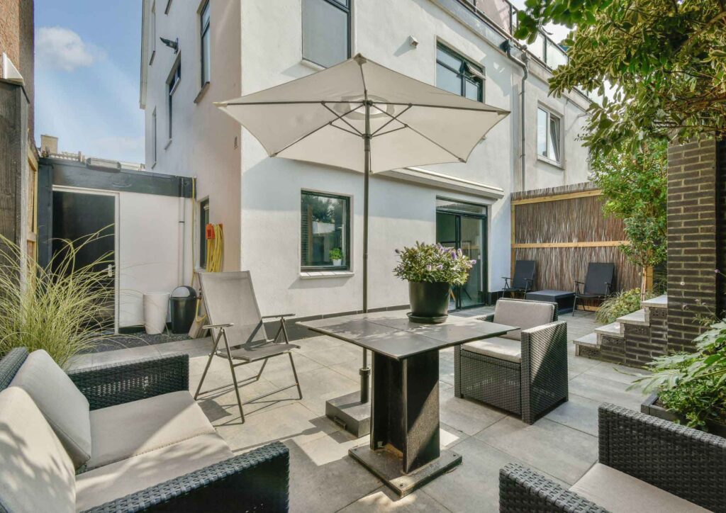 Spacious outdoor patio with a large patio umbrella providing shade over a cozy seating area, showcasing its ample coverage and stylish design. Perfect for relaxing in the garden, poolside, or patio, with lush greenery and modern furniture enhancing the outdoor atmosphere.