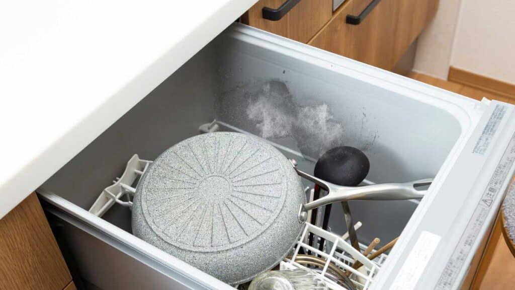 White hard water mineral buildup inside stainless steel dishwasher tub