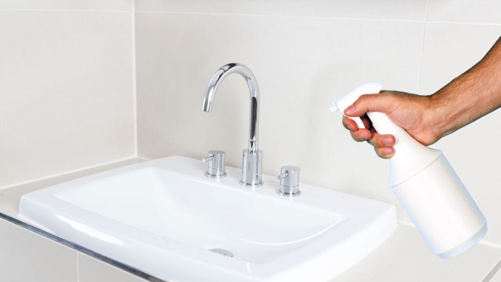 Spraying vinegar on bathroom sink faucet to remove hard water deposits