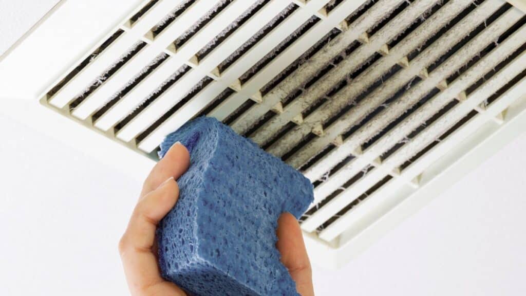 Cleaning bathroom exhaust fan blades and housing with brush and vacuum