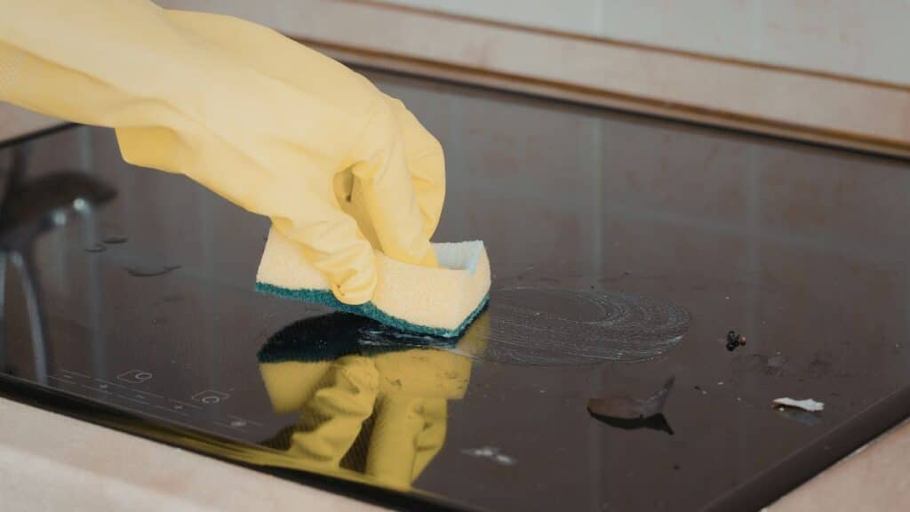 Black glass stove top being cleaned with microfiber cloth for streak-free shine