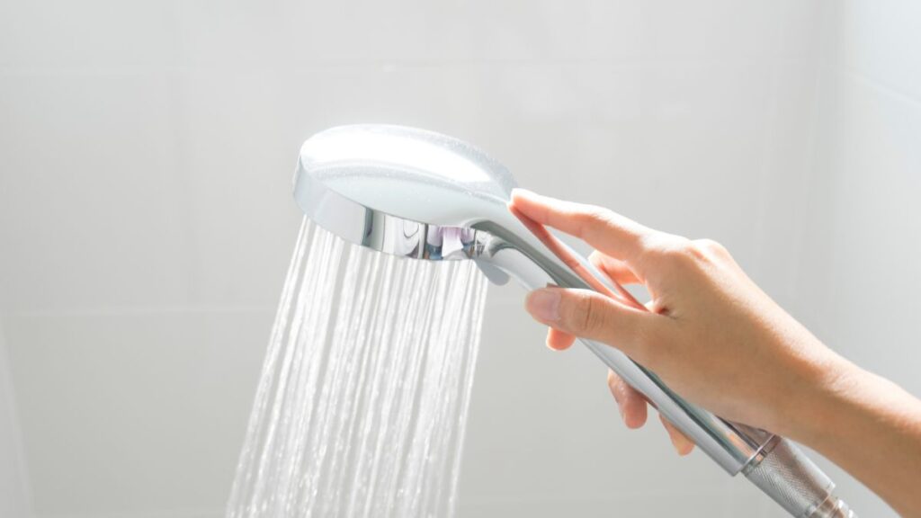 Rinsing shower walls with handheld shower head before cleaning