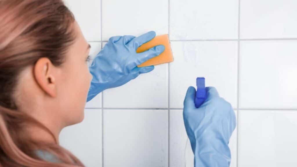person spraying bathroom cleaner on tile wall and wiping with cloth