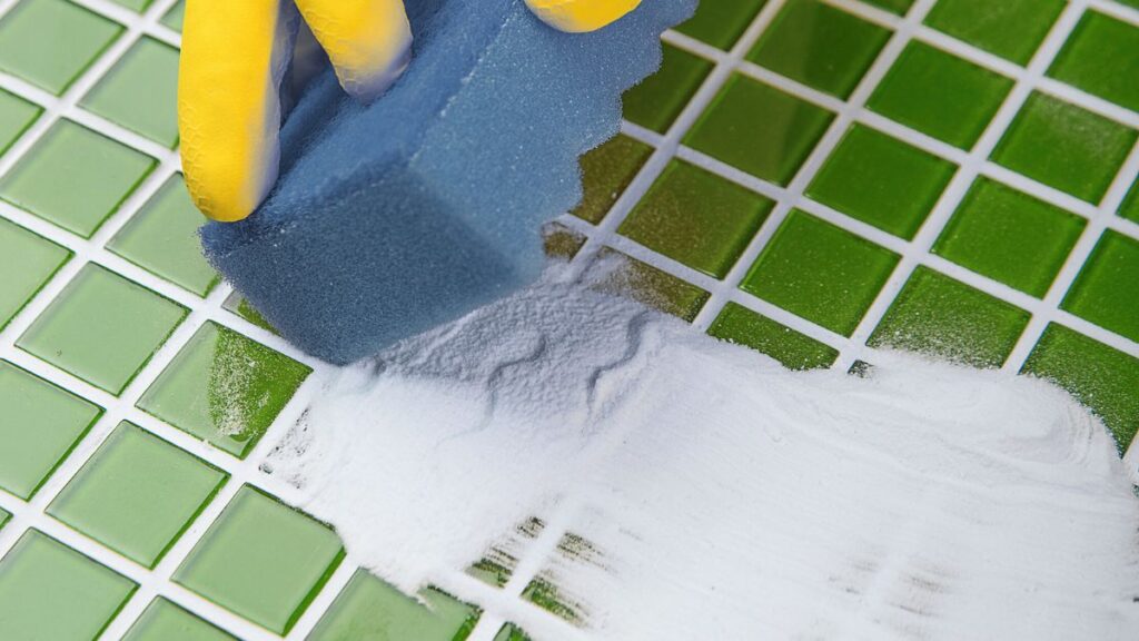 Scrubbing shower tile with baking soda to remove stubborn soap scum