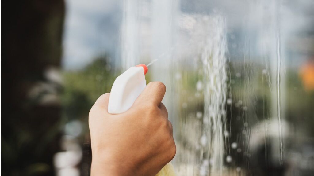 Spraying shower walls with vinegar and dish soap solution to remove soap scum