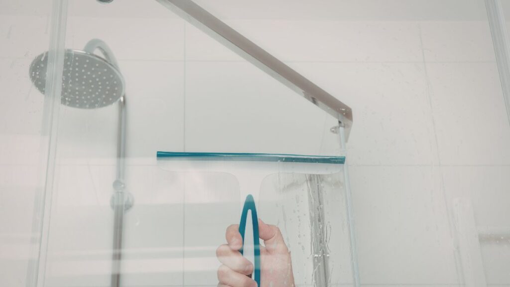 Using a squeegee on glass shower door to prevent water spots