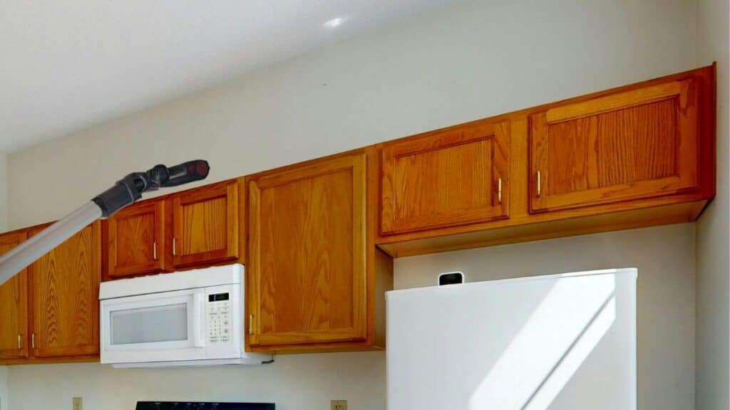 Vacuum removing dust and grease buildup from top of upper kitchen cabinets