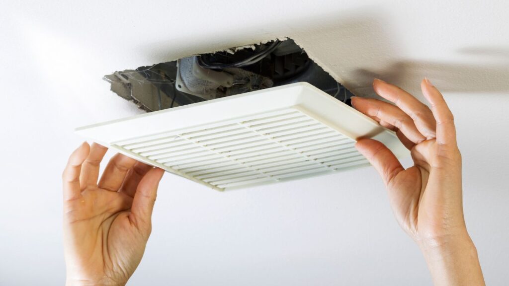 homeowner removing bathroom exhaust fan cover using spring clips